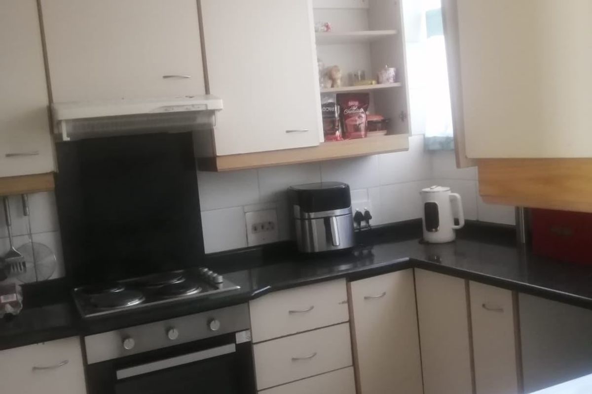 A functional kitchen featuring built-in cabinetry, laminate countertops, an electric hob, oven, and extractor fan with tiled flooring and backsplash.