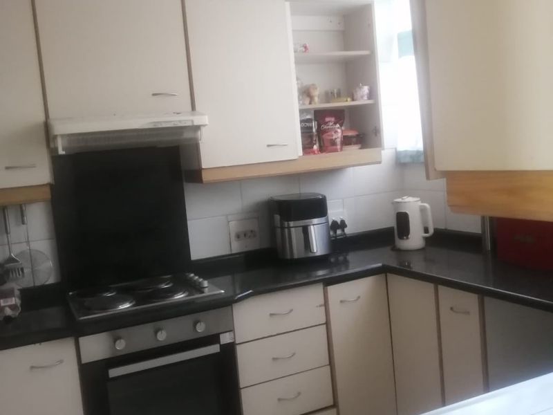 A functional kitchen featuring built-in cabinetry, laminate countertops, an electric hob, oven, and extractor fan with tiled flooring and backsplash.