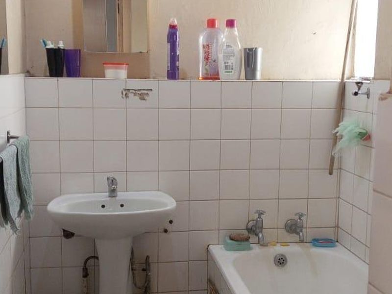 A functional bathroom featuring a pedestal basin, bathtub, and tiled finishes, currently requiring cosmetic updates and maintenance to improve its overall condition.