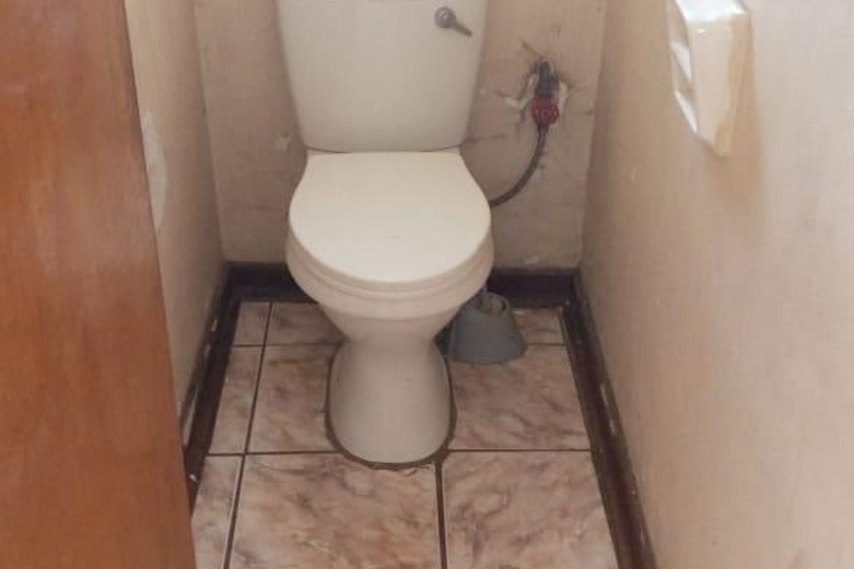 A small, dated bathroom featuring a standard toilet, ceramic floor tiles, and walls requiring cosmetic repair and maintenance.