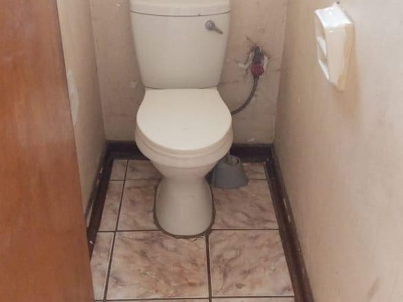 A small, dated bathroom featuring a standard toilet, ceramic floor tiles, and walls requiring cosmetic repair and maintenance.