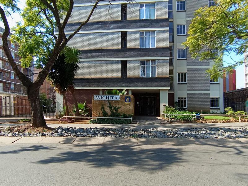 Street-facing view of the Wichita apartment complex, featuring a multi-story brick facade, secure gated entrance, and established trees.