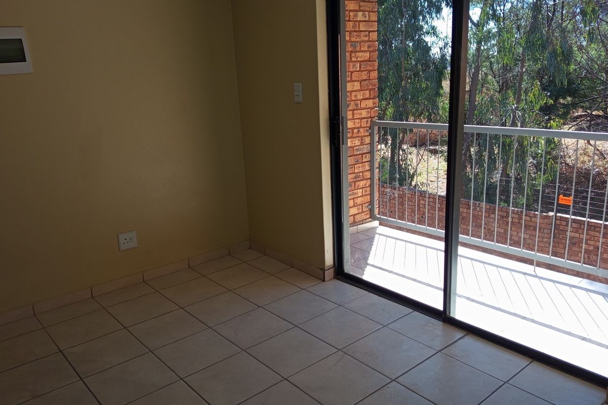 An empty living area featuring tiled flooring and a sliding glass door that opens onto a private balcony with metal railings.
