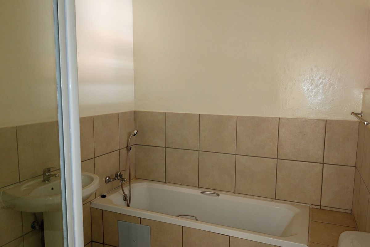 A functional bathroom featuring a bathtub with a handheld shower attachment, a pedestal basin, and neutral wall tiling.