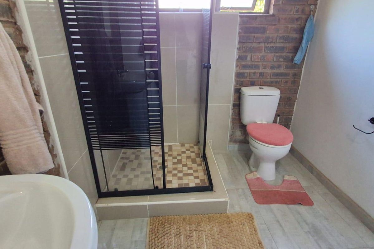 A bathroom featuring an exposed brick wall, a modern black-framed shower enclosure, and a standard toilet.