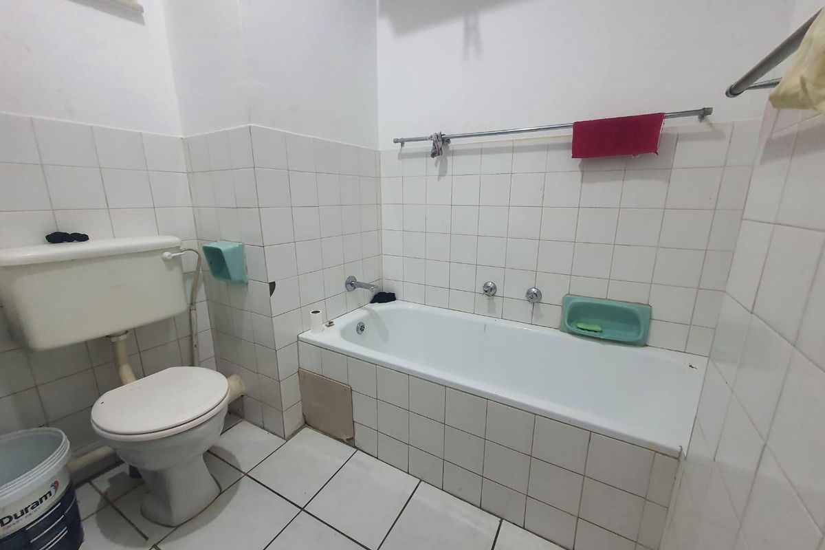 A dated bathroom featuring a standard bathtub, toilet, and white wall tiles. The space requires cosmetic updates and repairs to the tiled finishes.