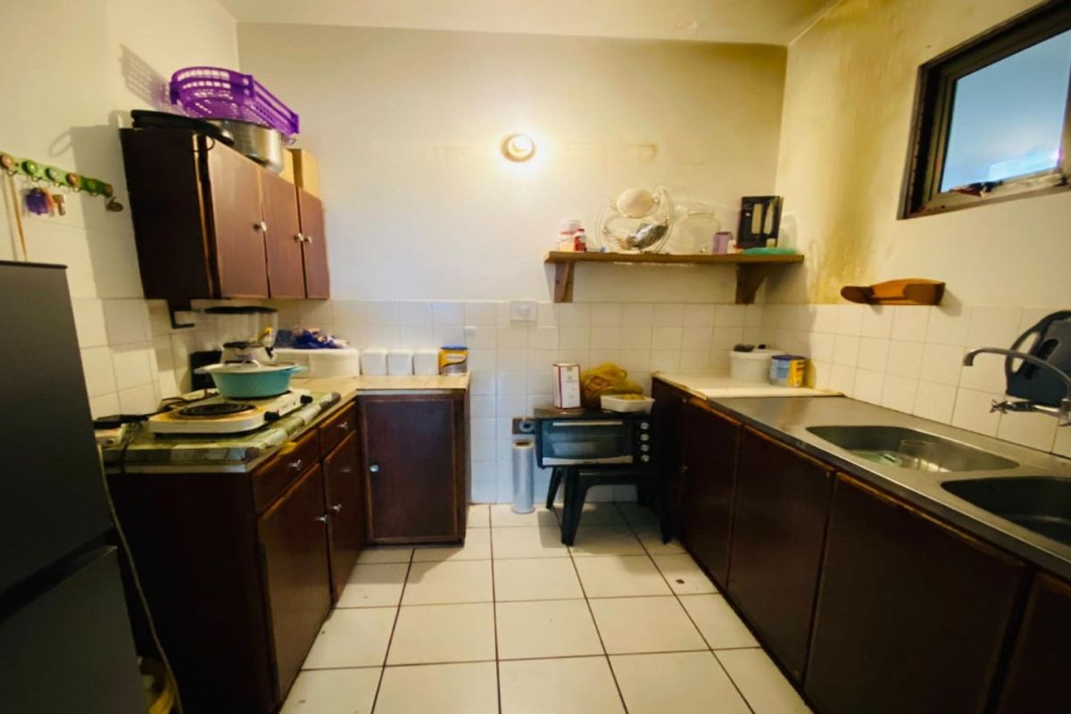 A dated kitchen featuring laminate cabinetry, tiled backsplash, and a double stainless steel sink, requiring cosmetic updates to modernize the space.