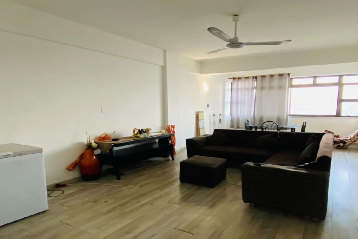 Spacious living room featuring light-toned laminate flooring, a ceiling fan, and large windows that provide ample natural light.