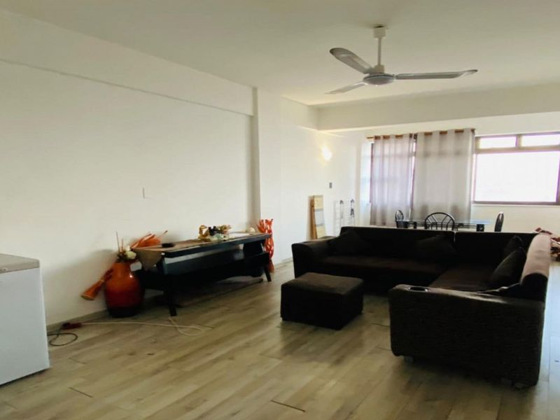 Spacious living room featuring light-toned laminate flooring, a ceiling fan, and large windows that provide ample natural light.
