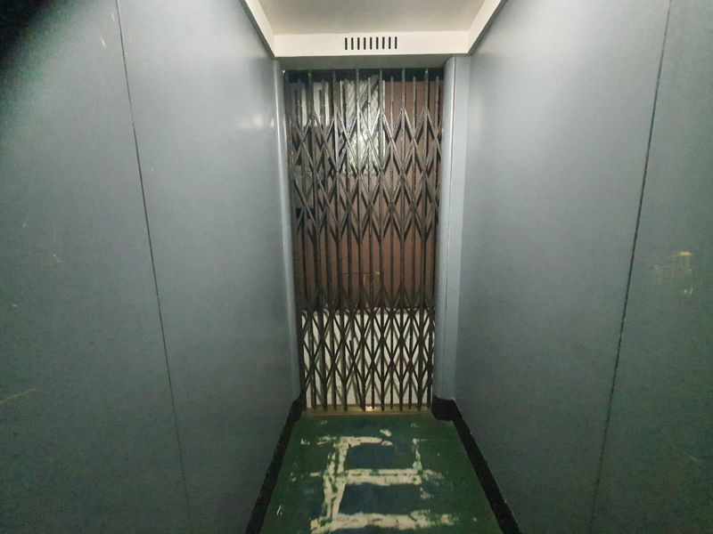 A narrow apartment hallway featuring an older style elevator with a metal scissor gate and worn flooring.