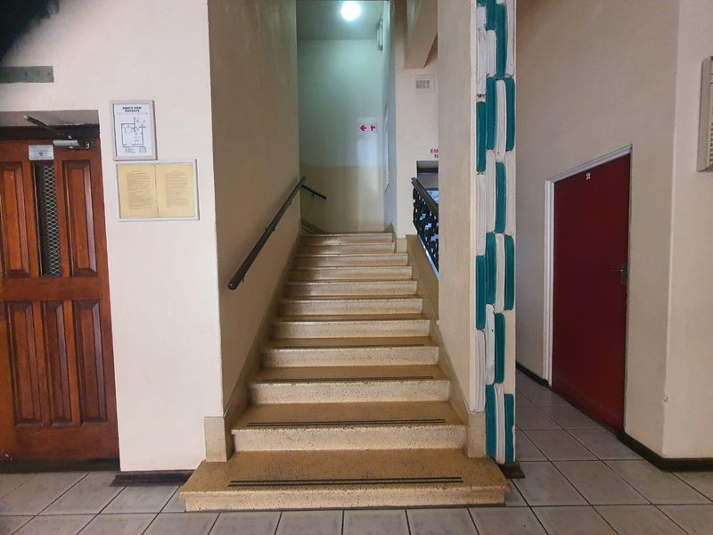 A communal apartment building hallway featuring a central staircase with handrails and tiled flooring, providing access to residential units.