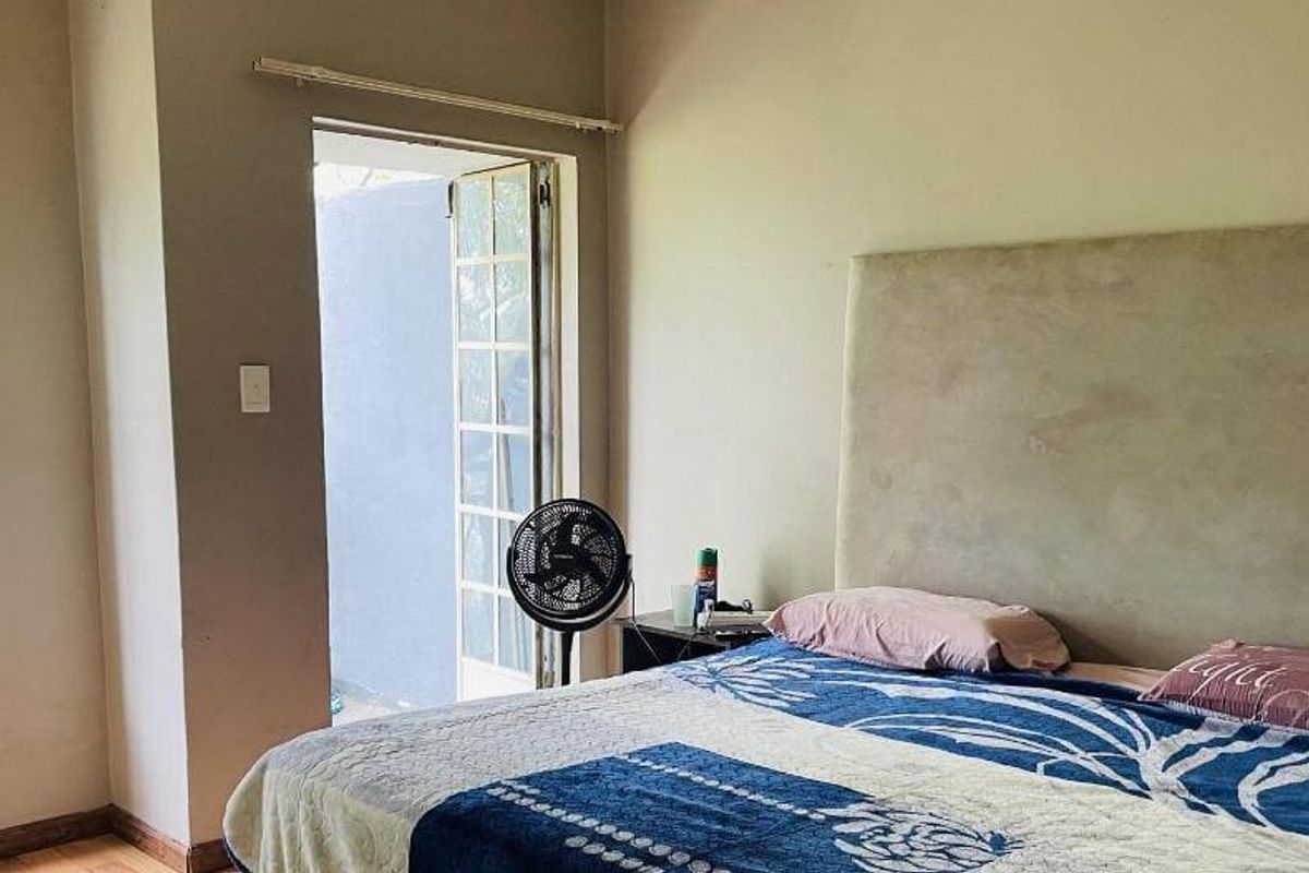 A bedroom featuring a large headboard, natural light from a casement window, and direct access to an outdoor area through french doors.