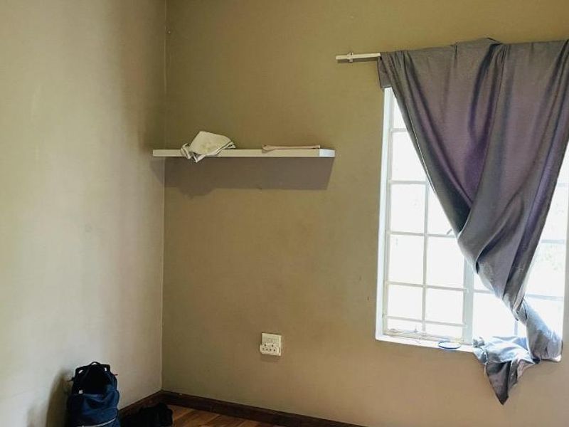 A vacant bedroom featuring laminate flooring, a wall-mounted shelf, and a window, requiring minor cosmetic updates to the wall finishes.