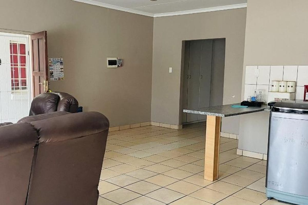 Open-plan living area featuring tiled flooring, a functional kitchen counter with built-in cabinetry, and direct access to the exterior via a security gate.