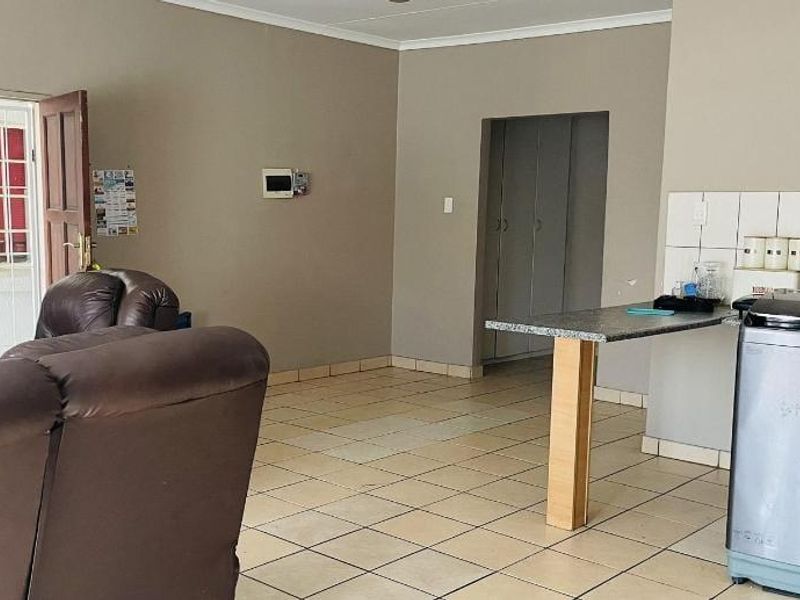 Open-plan living area featuring tiled flooring, a functional kitchen counter with built-in cabinetry, and direct access to the exterior via a security gate.