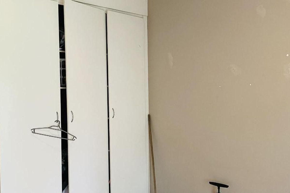 A bedroom featuring a built-in wardrobe with white folding doors and walls requiring cosmetic attention.