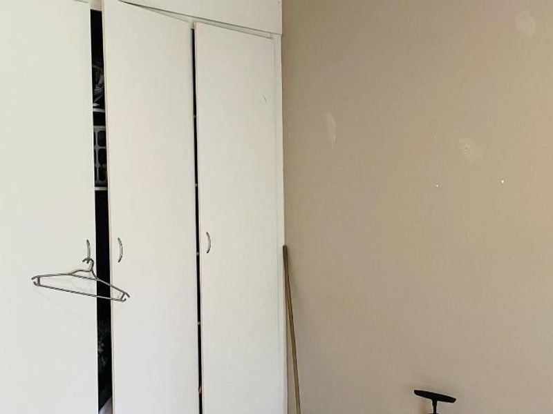 A bedroom featuring a built-in wardrobe with white folding doors and walls requiring cosmetic attention.