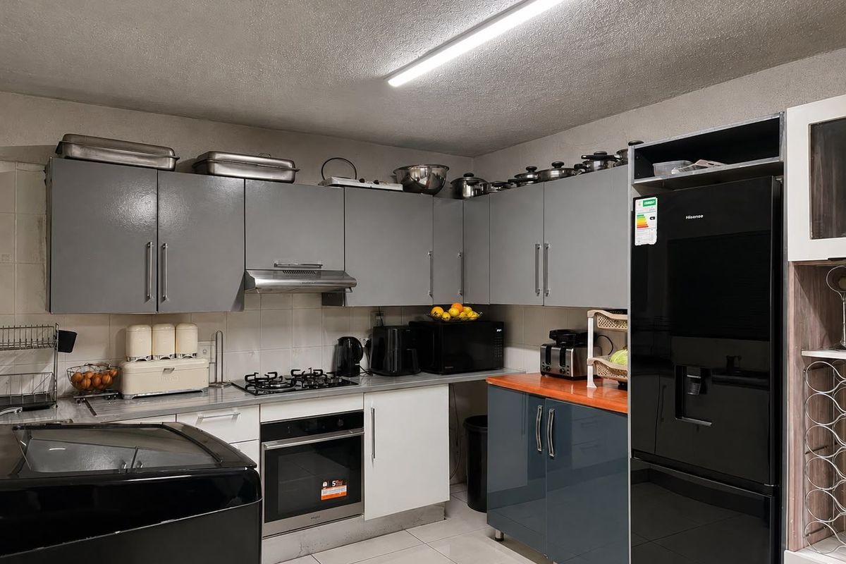 A functional kitchen featuring grey and white cabinetry, a gas hob, built-in oven, extractor fan, and tiled flooring with a modern aesthetic.