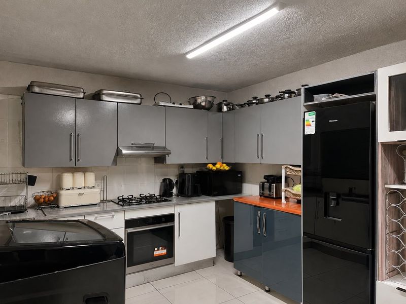 A functional kitchen featuring grey and white cabinetry, a gas hob, built-in oven, extractor fan, and tiled flooring with a modern aesthetic.