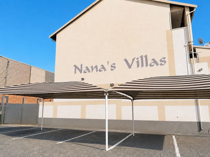 Exterior view of the Nana's Villas apartment complex featuring a paved parking area with striped shade cloth carports.