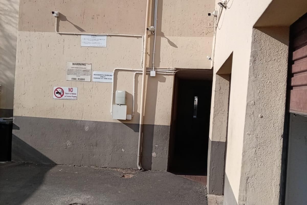 Exterior rear view of an apartment building showing paved parking area, security cameras, and building access point.