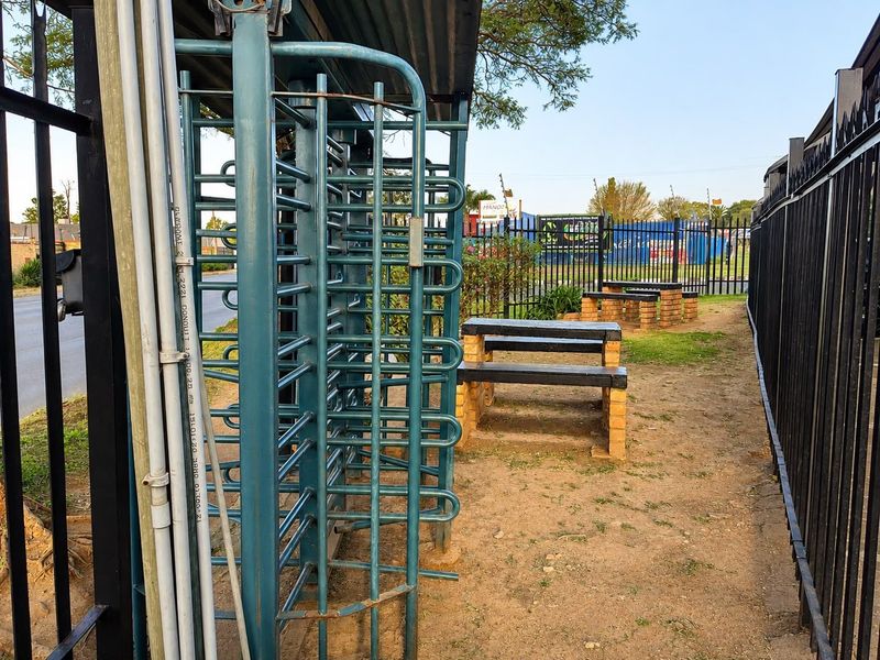Exterior entrance area featuring a metal turnstile, perimeter security fencing, and basic brick-based seating structures.
