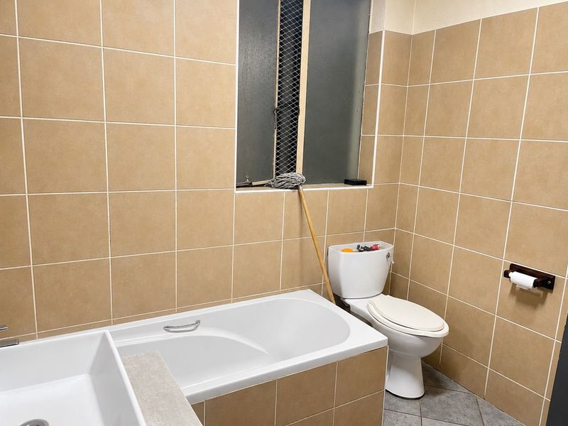 A functional bathroom featuring full-height wall tiling, a standard bathtub, and a toilet, with a frosted window providing natural light and privacy.