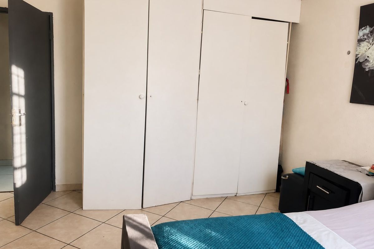 A bedroom featuring tiled flooring and built-in white cupboards, offering functional storage space within the apartment.