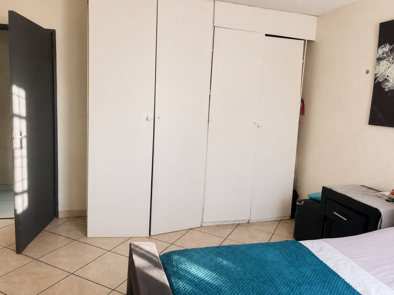 A bedroom featuring tiled flooring and built-in white cupboards, offering functional storage space within the apartment.