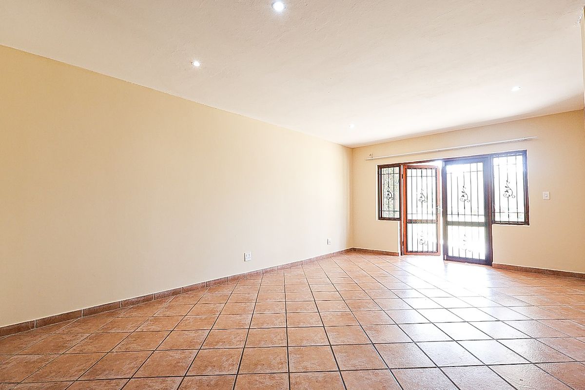 A spacious, empty living area featuring neutral walls, ceramic floor tiles, recessed lighting, and a secure sliding glass door leading to the exterior.