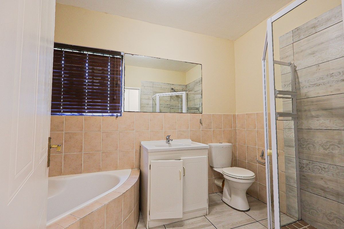 A functional bathroom featuring a corner bathtub, separate shower enclosure, vanity cabinet, and tiled finishes throughout.