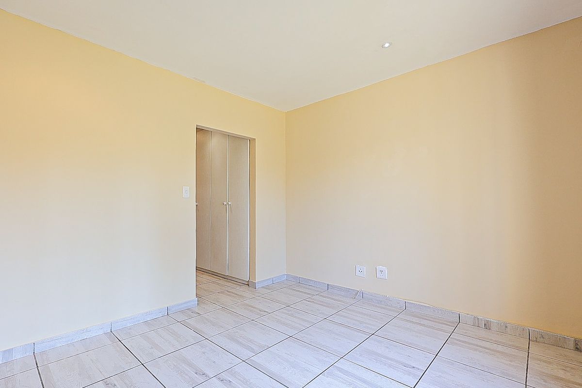 An empty bedroom featuring neutral wall paint, tiled flooring, and built-in cupboard storage.