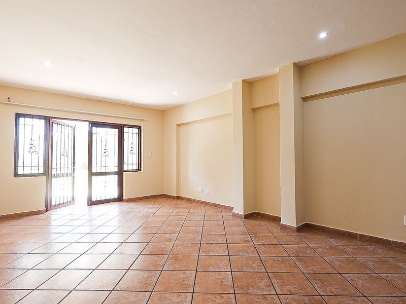 A spacious, empty living area featuring neutral walls, tiled flooring, recessed lighting, and a sliding glass door with an integrated security gate.