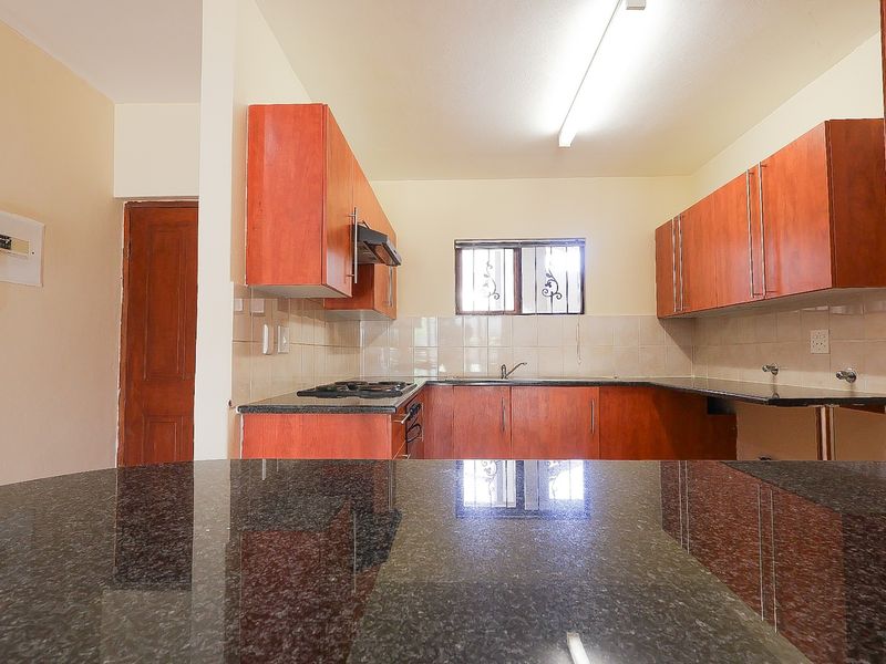 A functional kitchen featuring granite countertops, built-in wooden cabinetry, a tiled backsplash, and integrated cooking appliances.