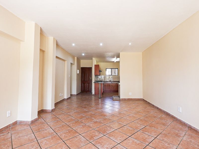 An open-plan living and kitchen area featuring tiled flooring, recessed lighting, and built-in kitchen cabinetry in a neutral, well-maintained space.