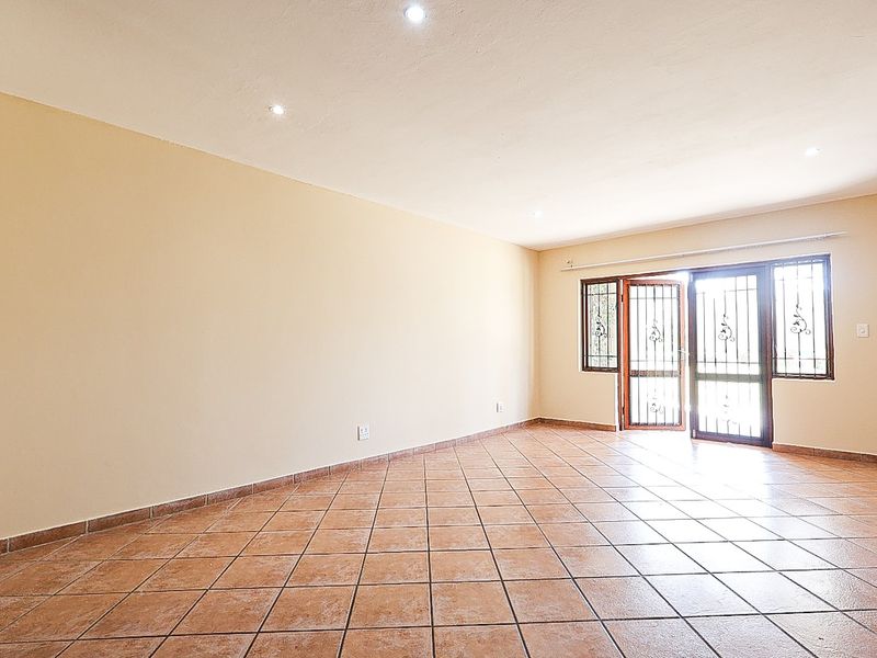 A spacious, empty living area featuring neutral walls, ceramic floor tiles, recessed lighting, and a secure sliding glass door leading to the exterior.