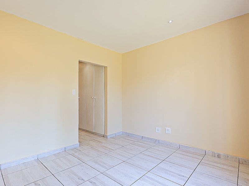 An empty bedroom featuring neutral wall paint, tiled flooring, and built-in cupboard storage.
