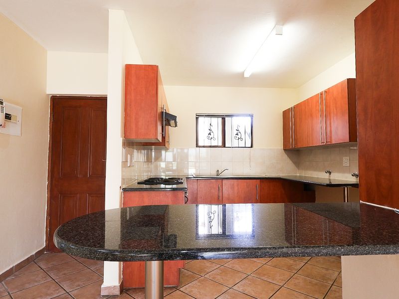 A functional kitchen featuring wooden cabinetry, granite countertops, a built-in hob, and tiled flooring, offering a practical layout for daily meal preparation.