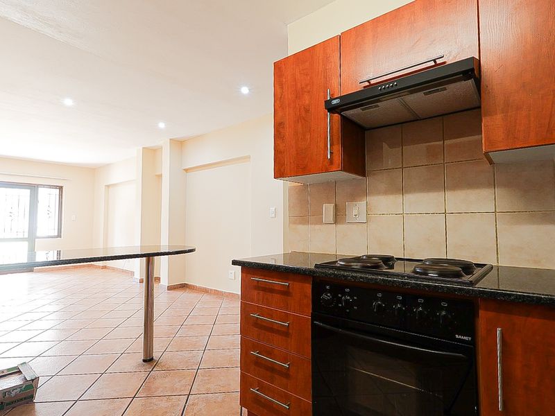 Open-plan kitchen and living area featuring wooden cabinetry, granite countertops, built-in oven and hob, and tiled flooring throughout.
