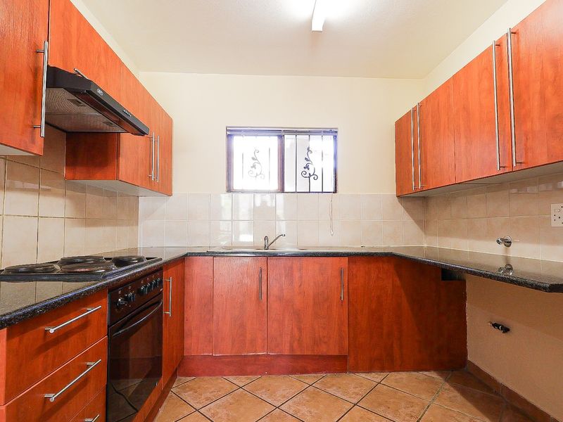 A functional kitchen featuring wood-finish cabinetry, granite countertops, a built-in electric stove with extractor fan, and tiled flooring.