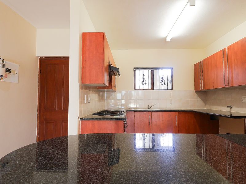 A functional kitchen featuring granite countertops, built-in wooden cabinetry, a gas hob with extractor fan, and a tiled backsplash.