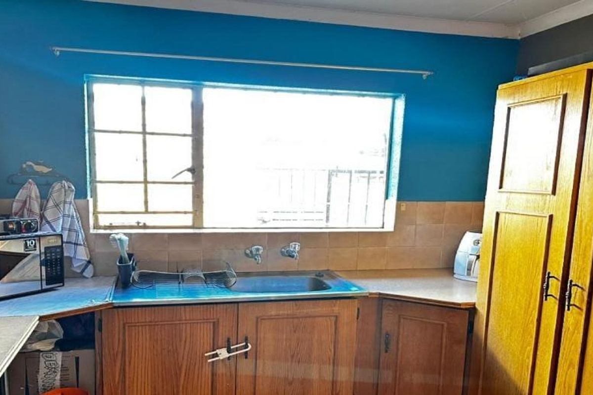 A functional kitchen featuring wooden cabinetry, laminate countertops, and a stainless steel sink, requiring cosmetic updates to modernize the space.