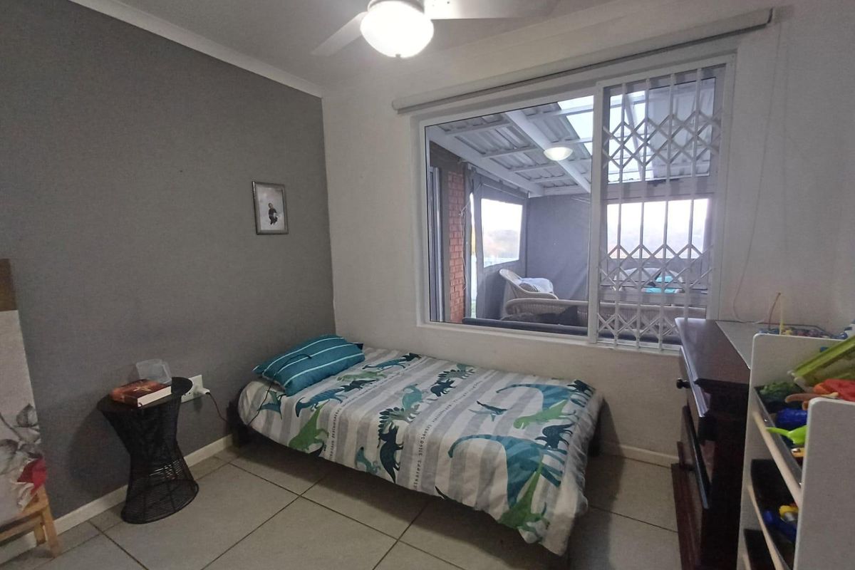 A bedroom featuring tiled flooring, a ceiling fan, and a window fitted with a security gate, overlooking an enclosed patio area.