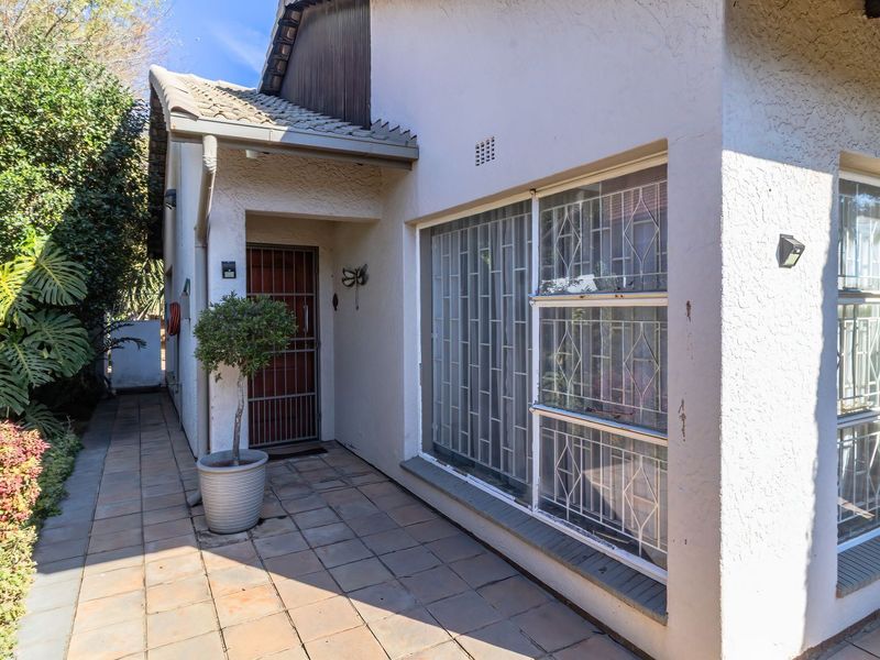 Front entrance area featuring a tiled patio, security gate, and windows with fitted security bars, set against a stucco-finished exterior wall.