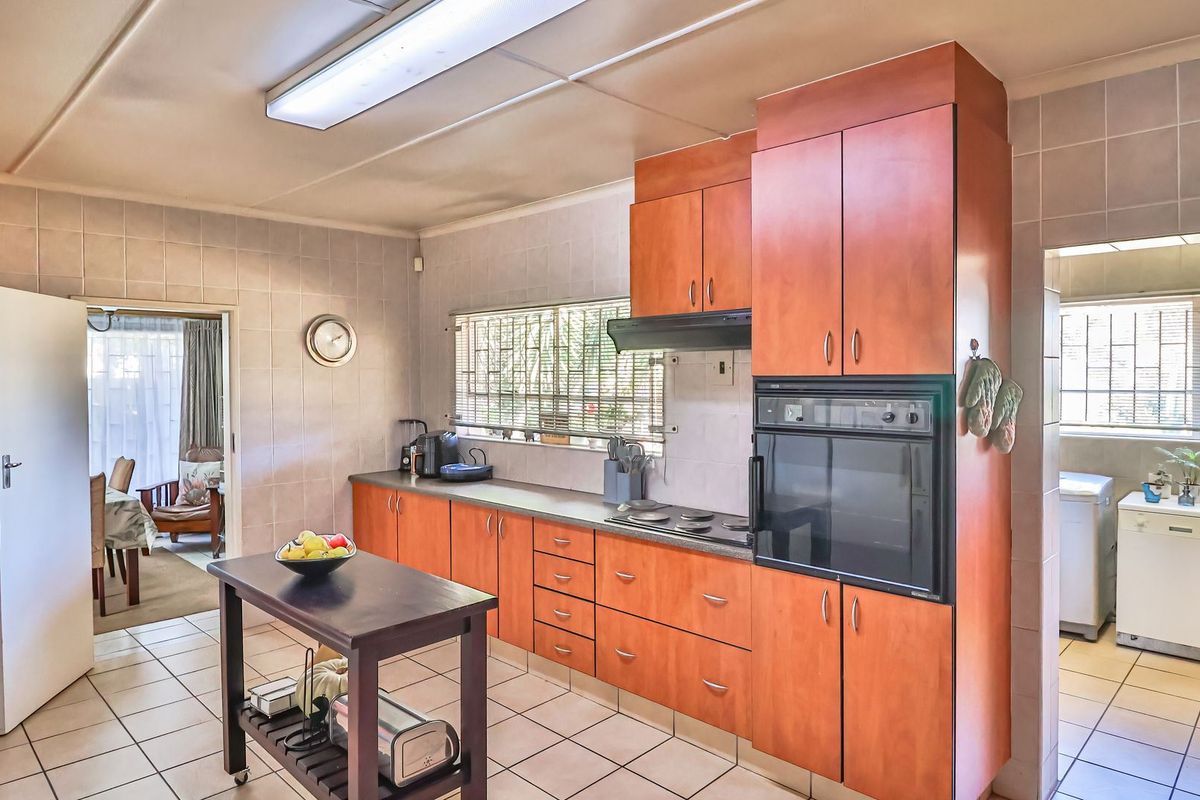 A functional kitchen featuring wood-finish cabinetry, built-in oven, electric hob, and tiled flooring, with an adjacent scullery area visible.