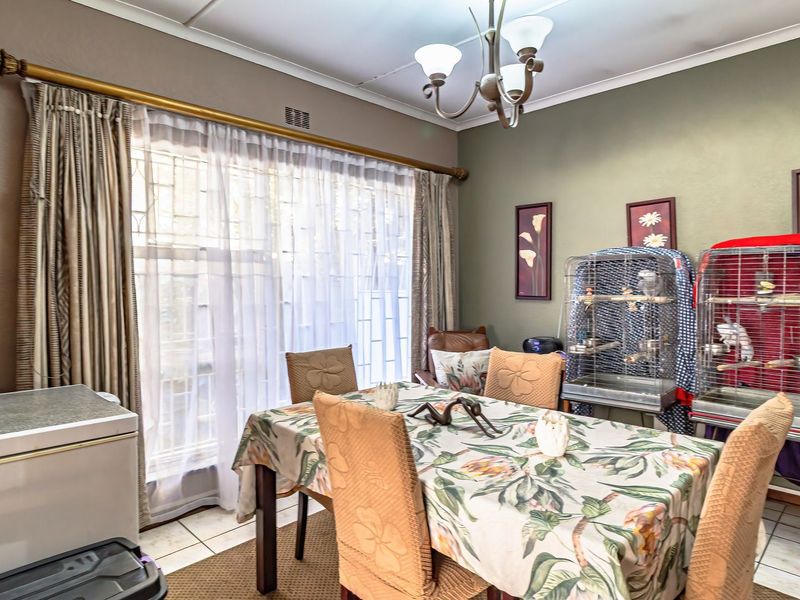 A dining room featuring tiled flooring, a central ceiling light fixture, and large windows with security gates.