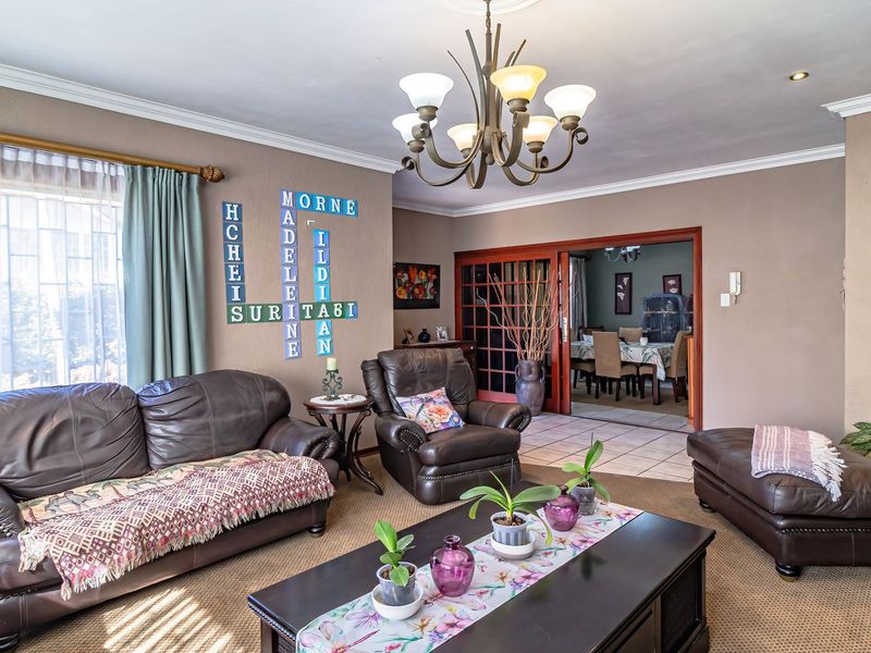 Spacious living room featuring a decorative chandelier, crown molding, and sliding glass doors leading to an adjacent dining area.