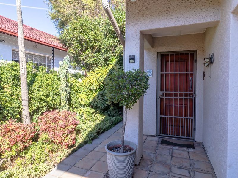 Front entrance area featuring a tiled porch, security gate, and well-maintained garden surroundings.