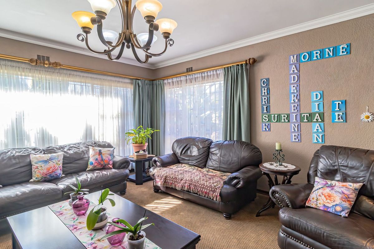 A comfortable living room featuring crown molding, large windows with curtain rods, and a central chandelier, providing a warm and inviting atmosphere.