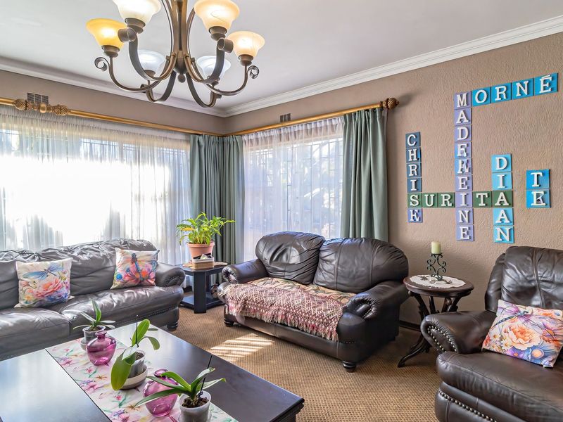 A comfortable living room featuring crown molding, large windows with curtain rods, and a central chandelier, providing a warm and inviting atmosphere.